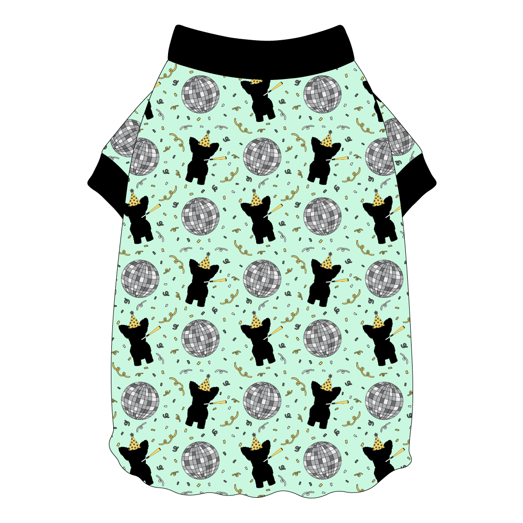 Tee shirt with flutter hem in a dog friendly pattern that shows a mirror ball, dog with a party blower and confetti on a light green background. It's complete with black trim on the neck and sleeves.