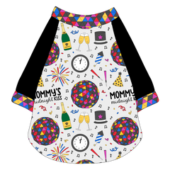 Raglan style tee in a dog friendly pattern that shows a multi-colored New Years ball, the words Mommy's Midnight Kiss, a clock, champagne bottle and champagne toast, fireworks, confetti and more on a white background. It's complete with black sleeves and trimmed in NYE Ball. NYE Ball trim is also on the neck and waist.