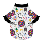 Tee style in a dog friendly pattern that shows a multi-colored New Years ball, the words Mommy's Midnight Kiss, a clock, champagne bottle and champagne toast, fireworks, confetti and more on a white background. It's complete with black ruffles on the sleeve edges. Black trim is also on the neck and waist.