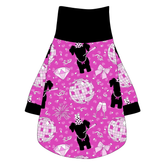 Tee shirt with turtleneck in a dog friendly pattern that shows a girl dog with hat and necklace, along with a mirror ball, champagne glasses, fireworks and confetti on a magenta cheetah print background. It's complete with black trim on the neck, sleeves and waist.