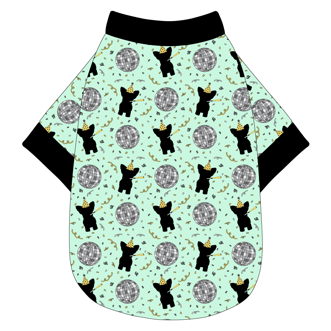 Tee shirt in a dog friendly pattern that shows a mirror ball, dog with a party blower and confetti on a light green background.  It's complete with black trim on the neck, waist and sleeves