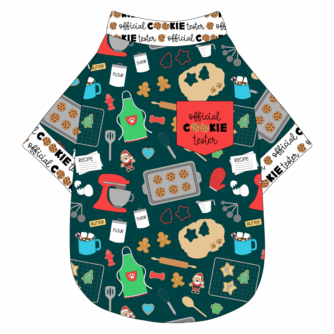 Tee shirt in a dog friendly pattern that shows cookies baking, a light green apron, recipe cards and more on a deep emerald background. It's complete with official cookie tester trim on the neck, waist and sleeves, as well as a red pocket that reads Official Cookie Tester.