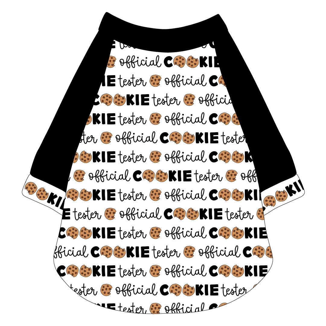 Raglan style tee in a dog friendly pattern that shows the text Official Cookie Tester, using two cookies for letter “o” in cookies, on a white background. It's complete with black sleeves and trimmed in official cookie tester. Black trim is also on the neck and waist.