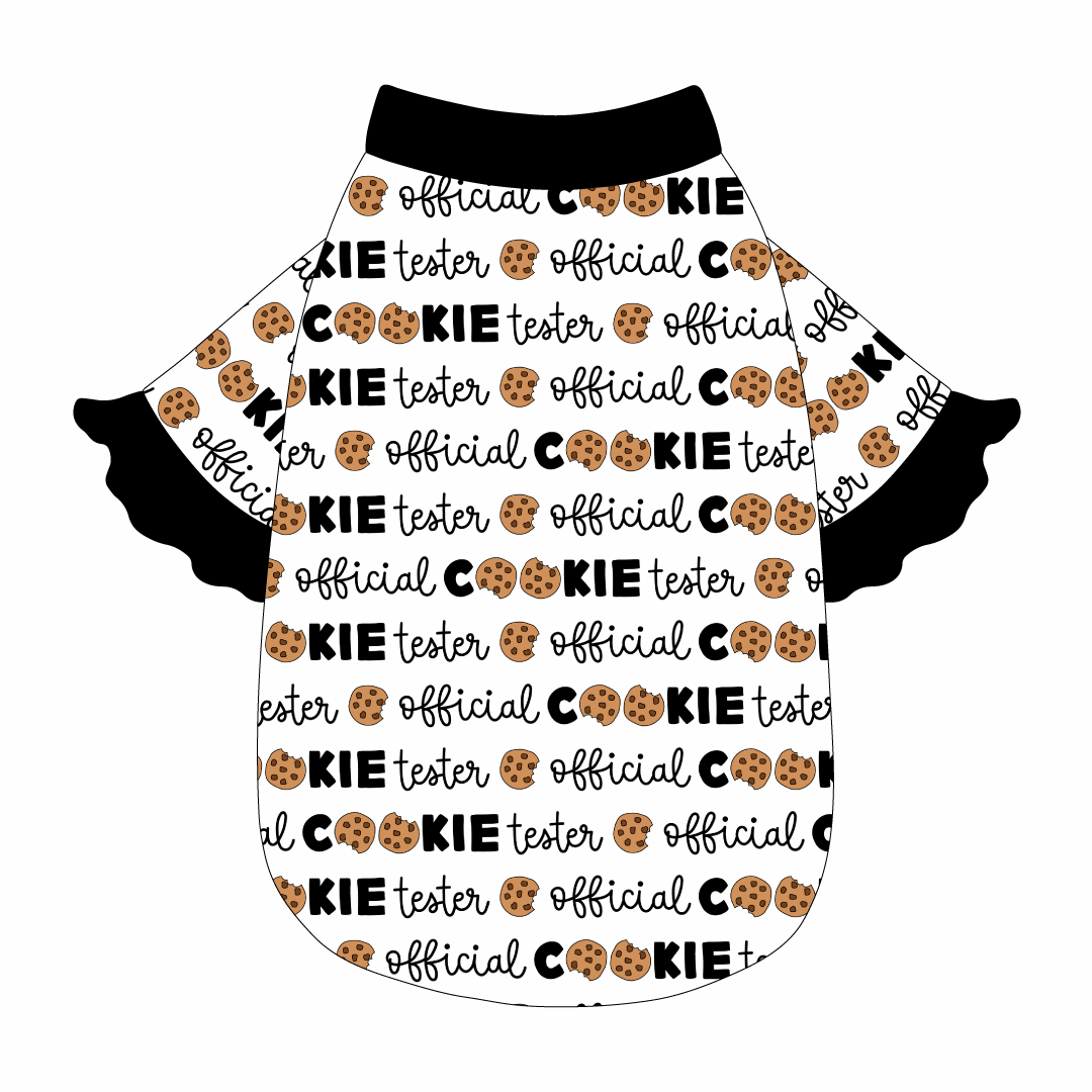 Tee style in a dog friendly pattern that shows the text Official Cookie Tester, using two cookies for letter “o” in cookies, on a white background. It's complete with black ruffles on the sleeve edges. Black trim is also on the neck and waist.