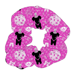 Scrunchie hair accessory in a dog friendly pattern that shows a girl dog with hat and necklace, along with a mirror ball, champagne glasses, fireworks and confetti on a magenta cheetah print background.