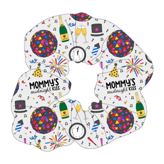 Scrunchie hair accessory in a dog friendly pattern that shows a multi-colored New Years ball, the words Mommy's Midnight Kiss, a clock, champagne bottle and champagne toast, fireworks, confetti and more on a white background.  It's complete with black trim on the neck, waist and sleeves.